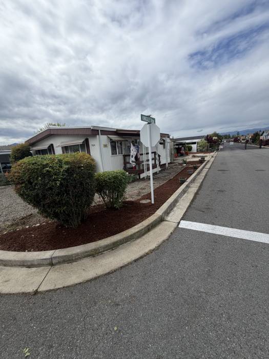 Corner-lot planting bed topped with fresh bark mulch and neatly rounded shrubs following a curved concrete curb in a Grants Pass, Oregon neighborhood.