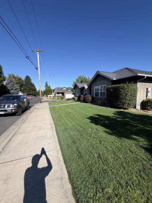 Front lawn mowed and sharply edged along the sidewalk at a dark-sided home on a residential street in Grants Pass, Oregon.